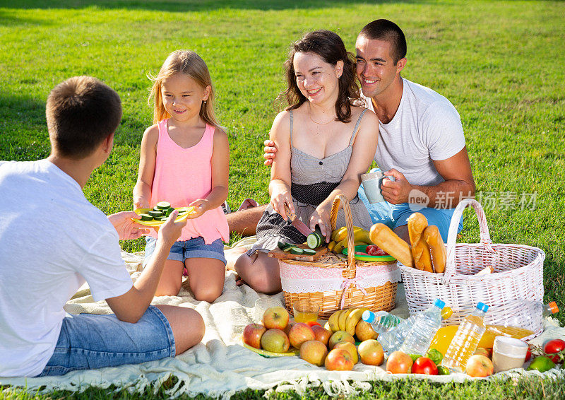 Happy parents with two kids having picnic together on green meadow in park